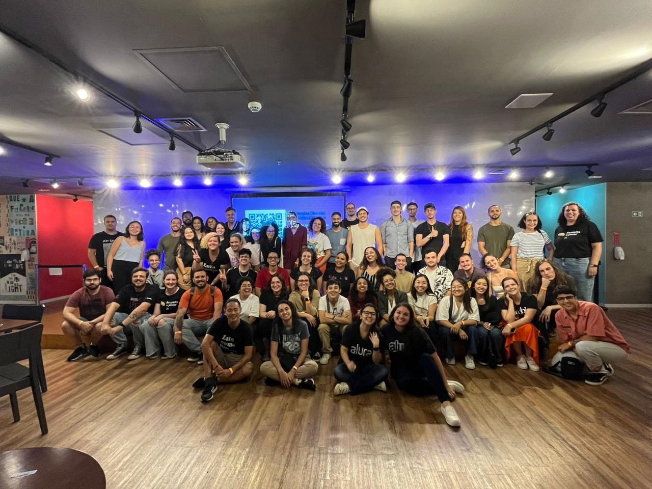 Grupo grande da comunidade VagasUX posando em um salão com palco ao fundo.