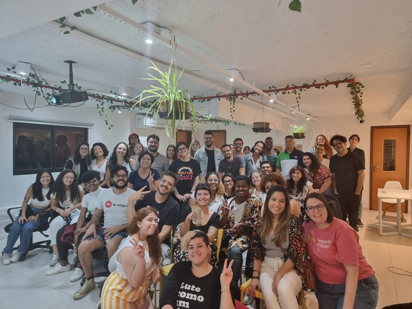 Grupo da comunidade VagasUX reunido em uma sala com plantas no teto.